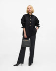 MiLA Boutique black cotton shirt with pointed collar and gold KARL lettering snap buttons, split side seams. Model holds a black KARL handbag.