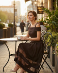 MiLA Boutique off-the-shoulder midi dress in dark brown with lace trim on the hem, worn by a woman sitting at a cafe.