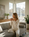 MiLA Boutique cream V-neck sweater with raglan sleeves and rib-knit trims, worn by a woman sitting on a sofa.