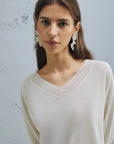 MiLA Boutique cream V-neck sweater with raglan sleeves and fine rib-knit trim. Model wears statement earrings.