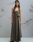 MiLA Boutique browncrinkle twill maxi dress with scoop neck, fabric belt, and flower detail. Model wears a flowing, asymmetrical hem dress.