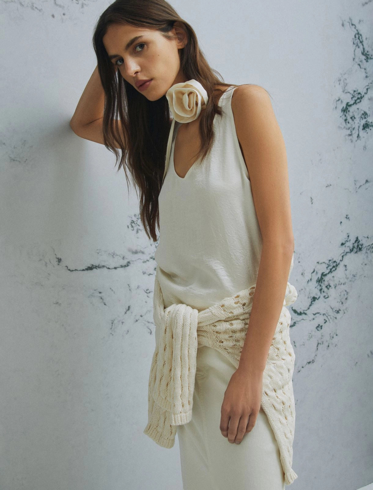 MiLA Boutique cream crinkle twill sleeveless top with V-neck and fabric flower accent. Model wears a cream cable knit sweater tied around waist.