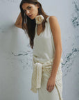 MiLA Boutique cream crinkle twill sleeveless top with V-neck and fabric flower accent. Model wears a cream cable knit sweater tied around waist.
